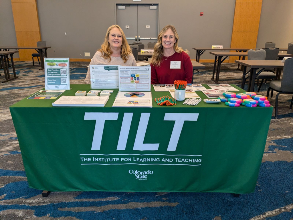 Two TILT staff members sit at a resource table at the annual POD conference