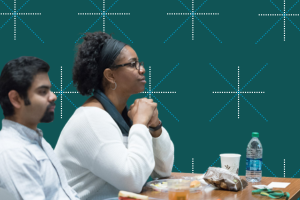 Two student sit at a table with snacks on it while listening to a workshop presentation